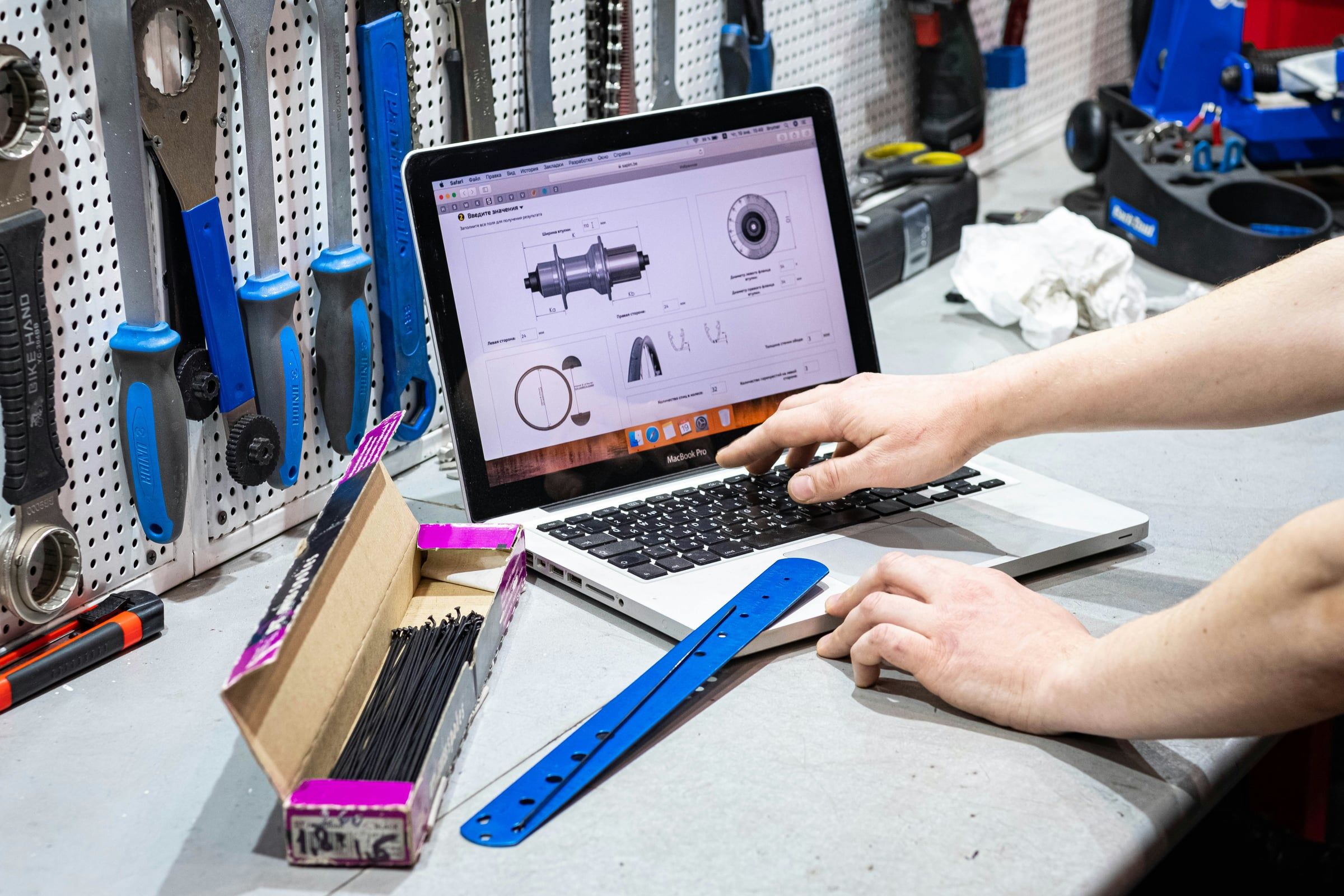 Un artisan consulte un ordinateur portable sur son établi, devant un panneau d'outils