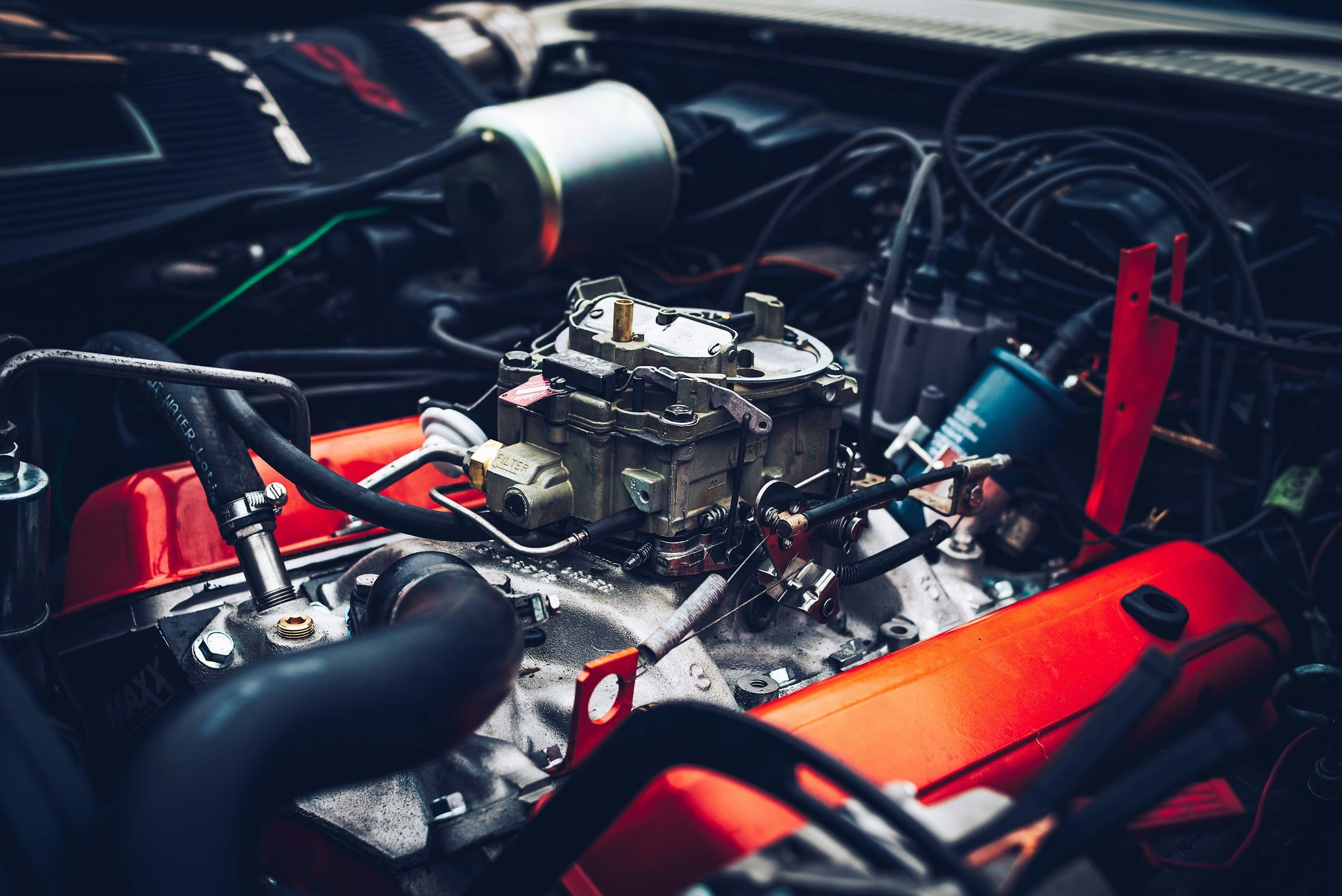 Le moteur d'une voiture, capot ouvert, avec son carburateur et ses câbles